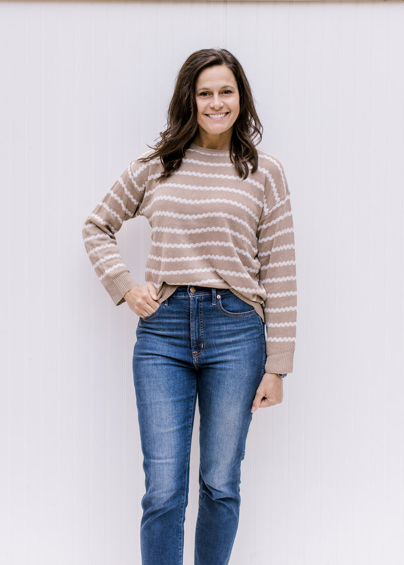 Model wearing jeans with a taupe long sleeve sweater with cream zig zag stripes and zipper on back.