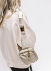 Model with a gold and taupe belt bag with an adjustable strap and zipper pockets over her shoulder. 