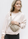 Model wearing a cross body gold and taupe bag with an adjustable strap and three zipper pockets. 