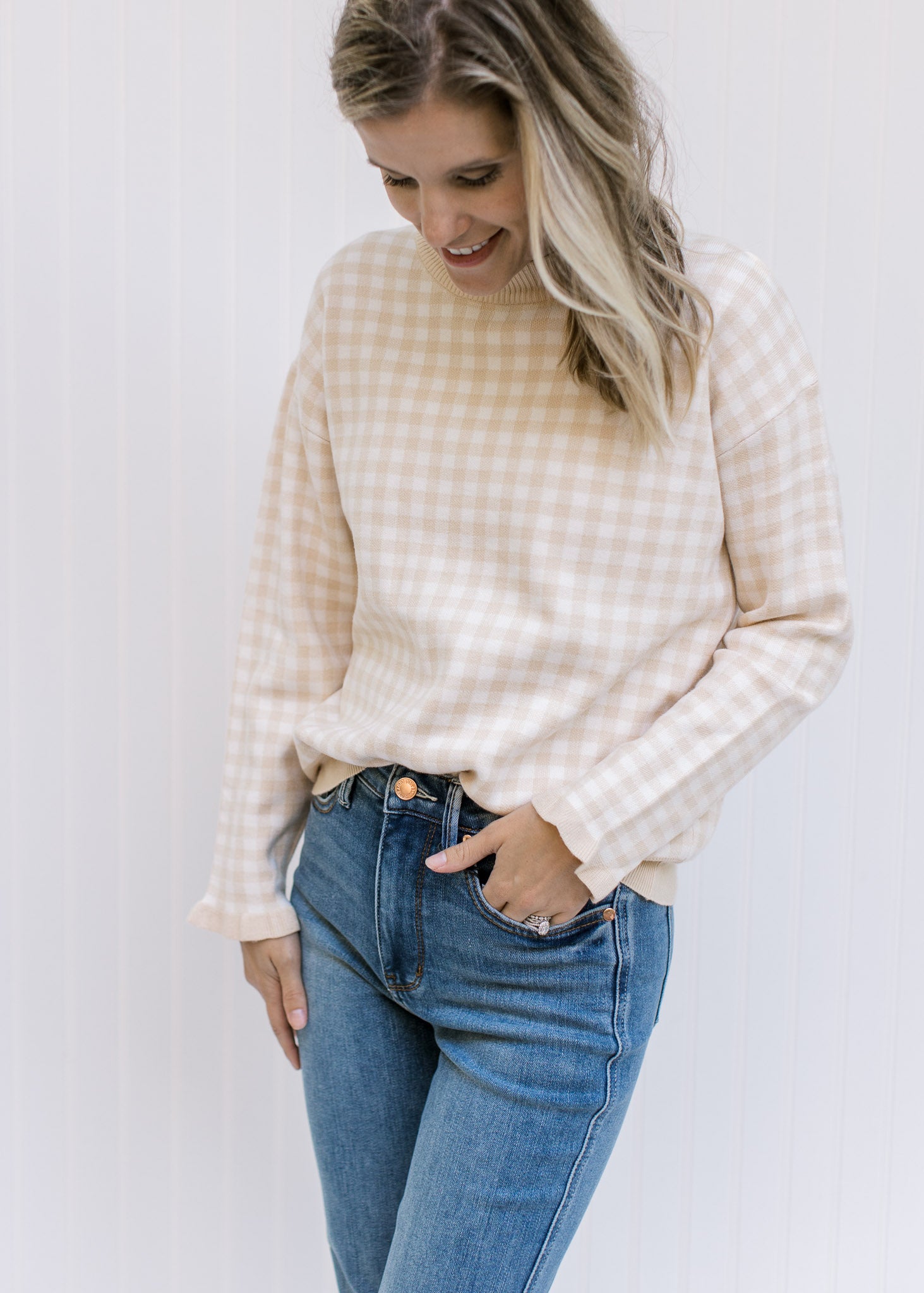 Model wearing jeans with a taupe and white checkered sweater with long sleeves and a round neck. 