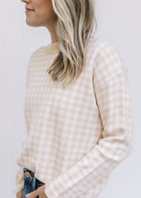 Model wearing a long sleeve taupe and white checkered sweater with ribbed neck, hem and cuff. 