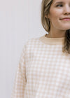 Close up of a taupe and white checkered sweater with long sleeves and a round neckline. 