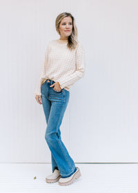 Model wearing a taupe and white checkered sweater with long sleeves and a round neckline. 