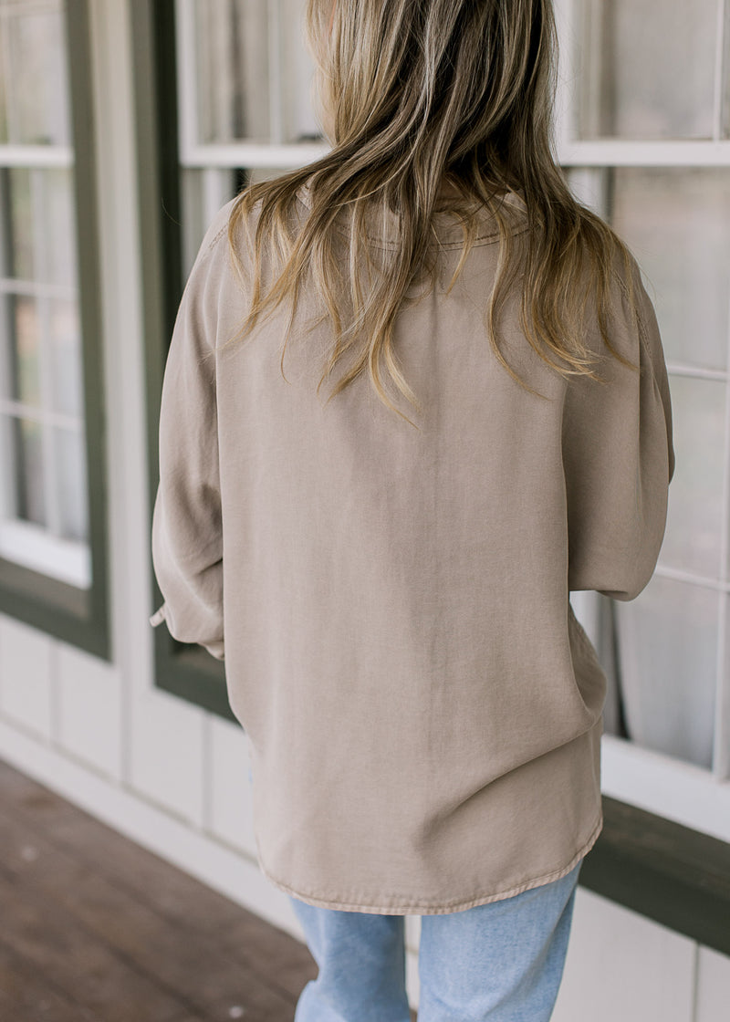 Back view of Model wearing a taupe button down top with patch pockets and long sleeves.