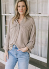 Model wearing jeans and a taupe button down top with patch pockets and long sleeves.