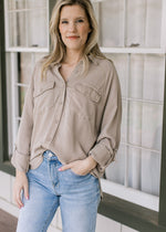 Model wearing jeans and a taupe button down top with patch pockets and long sleeves.