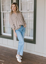 Model wearing sneakers, jeans and a taupe button down top with patch pockets.