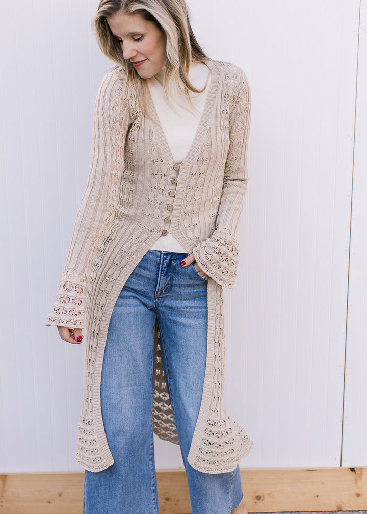 Model wearing a taupe crochet duster cardigan with long belle sleeves, v-neck with button closure.