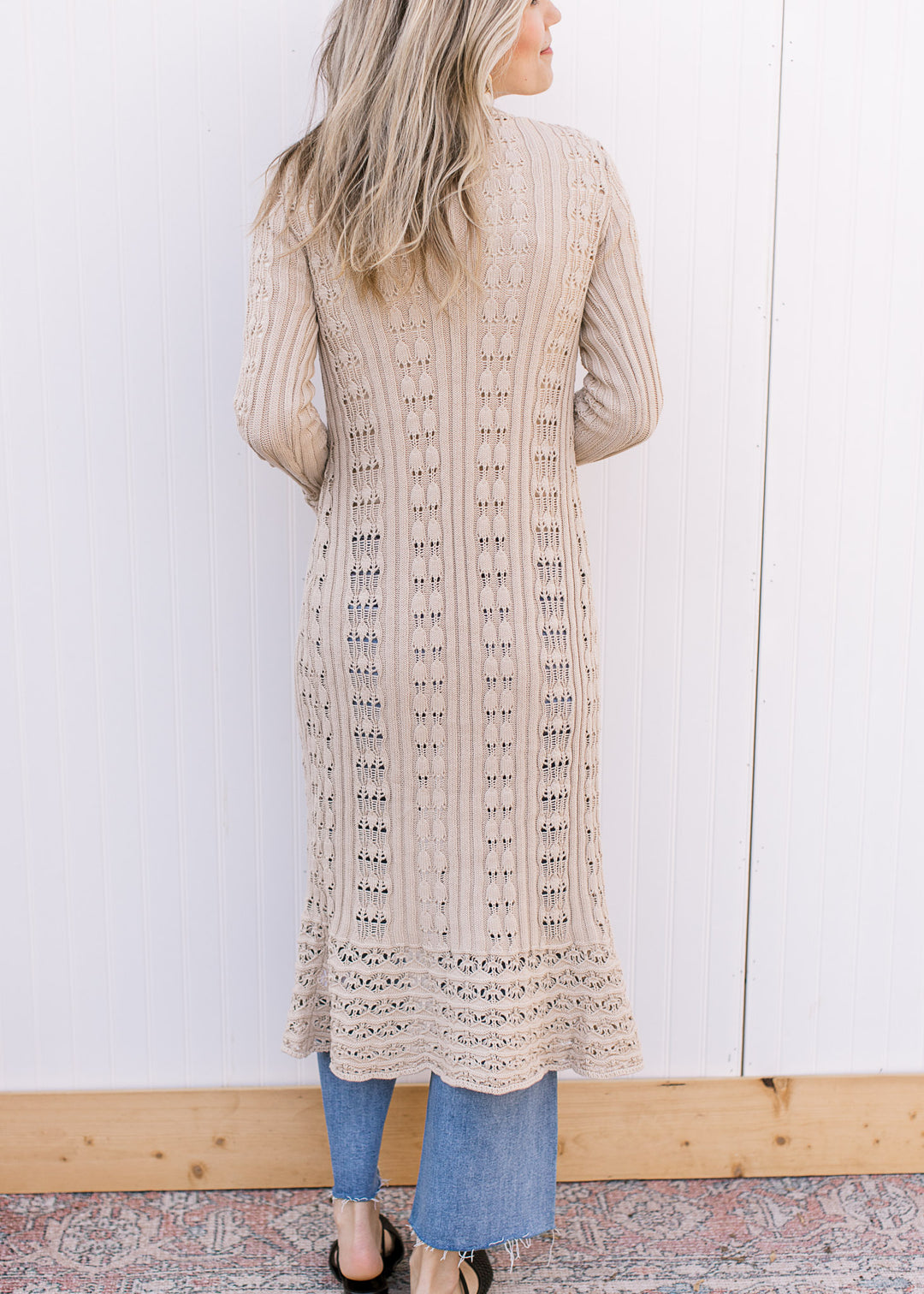 Back view of Model wearing a taupe crochet cardigan with long belle sleeves and v-neck with button.