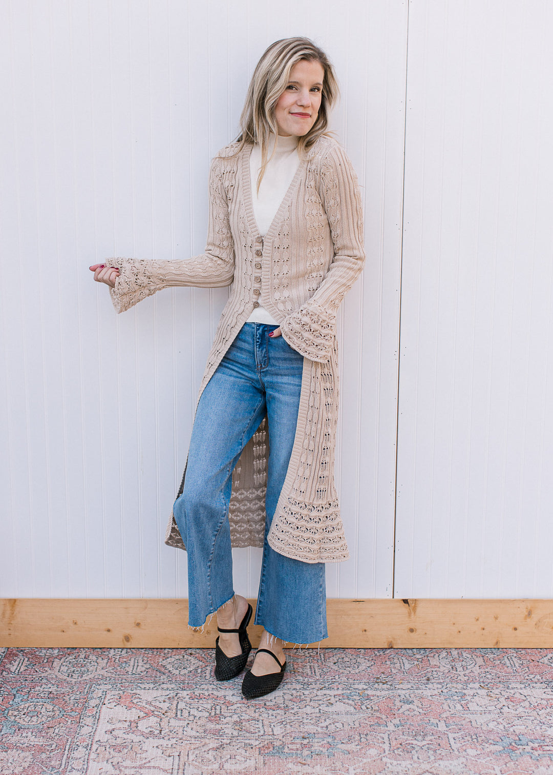 Model wearing jeans, flats and a taupe crochet cardigan with long belle sleeves and duster length.