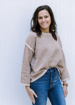 Model wearing a taupe sweater with cream hem lines, rolled hem, dropped shoulder and long sleeves. 