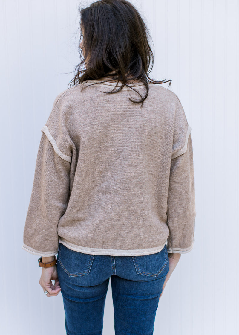 Back view of Model wearing a taupe sweater with cream hem lines, rolled hem and long sleeves. 
