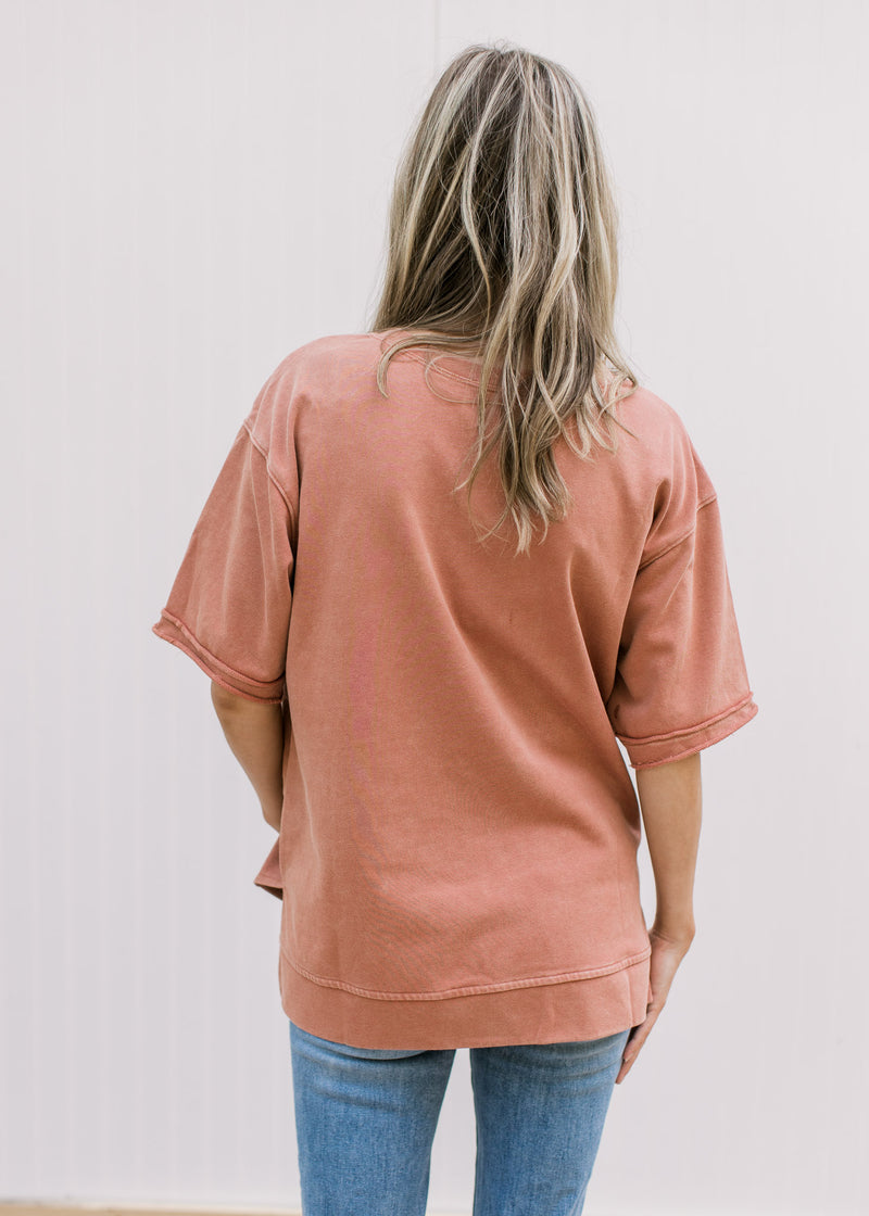 Back view of Model wearing a dusty peach top with a cream flower, short sleeves and a split hem.