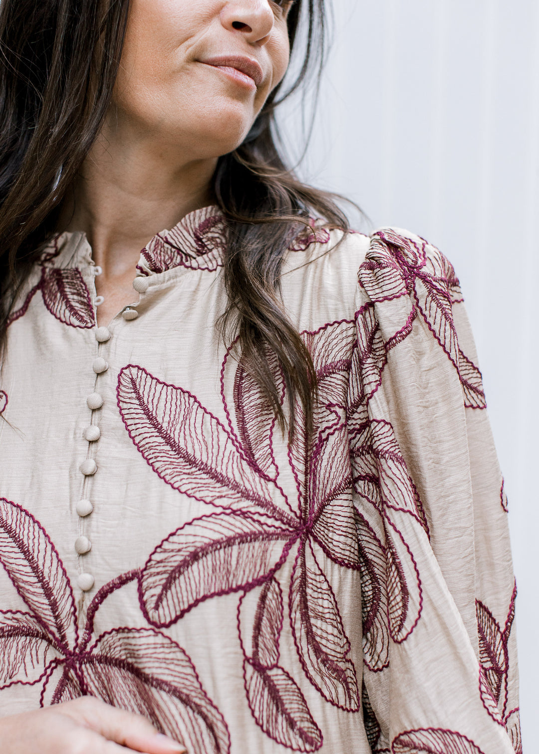 Close-up of taupe dress showing burgundy floral embroidery, ruffled mock neckline, covered buttons and pleated shoulder.