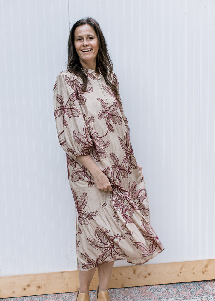 Model holding taupe embroidered midi skirt, showing burgundy floral motifs, bubble sleeves and flowing ruffled hem.