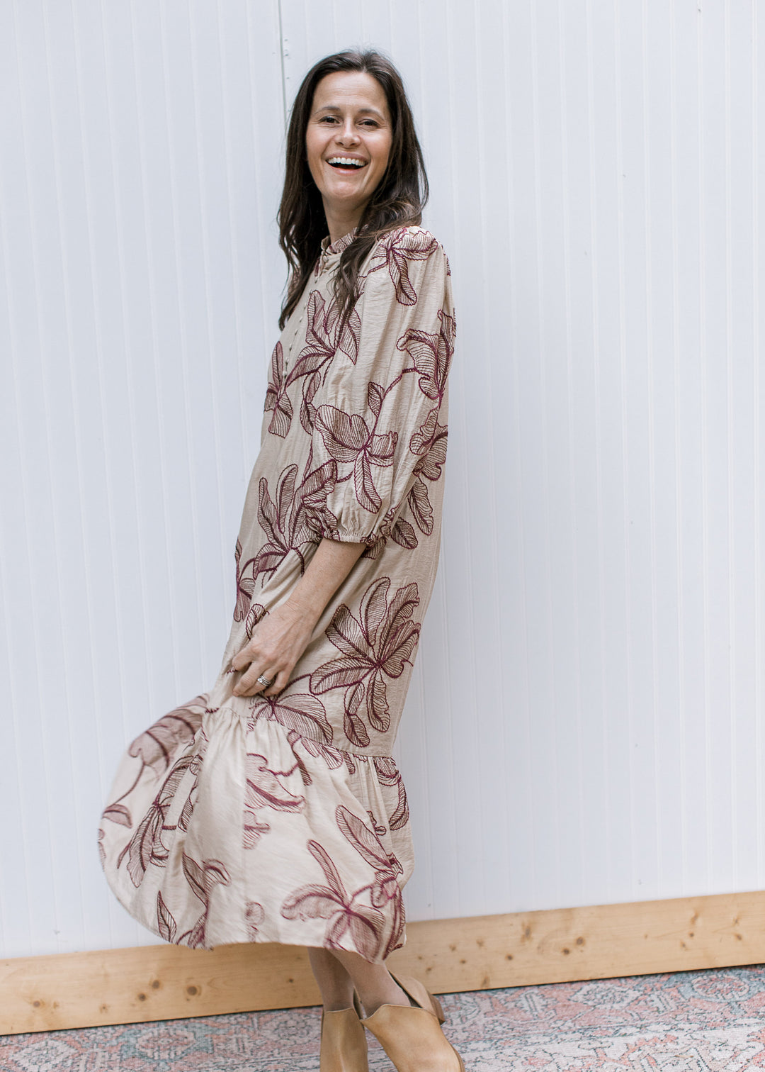 Side view of taupe midi dress with burgundy floral embroidery, three-quarter bubble sleeves and a swaying ruffled hem.
