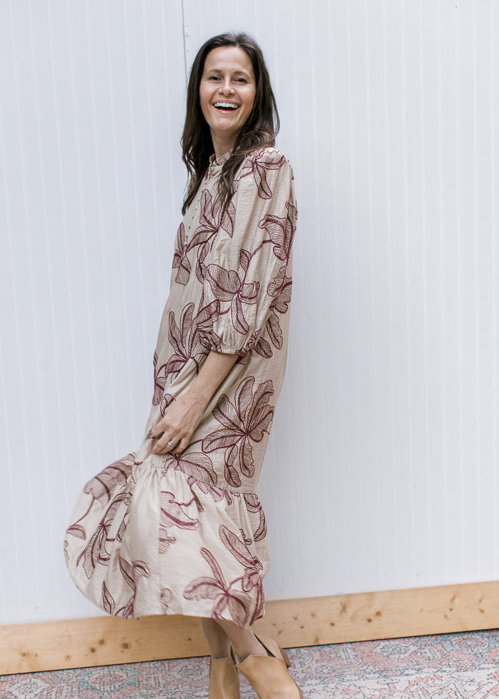 Side view of taupe midi dress with burgundy floral embroidery, three-quarter bubble sleeves and a swaying ruffled hem.