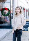 Model wearing a taupe top with a square neck, eyelet lace detail at neck and 3/4 sleeves. 