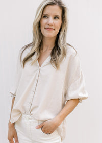 Model wearing a taupe button up top with 3/4 elastic sleeves and a collar. 