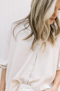 Close up of buttons on a taupe linen top with 3/4 sleeves with elastic. 
