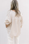 Back view of Model wearing a taupe button up top with 3/4 elastic sleeves and a collar.