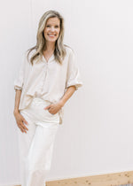Model wearing white pants with a taupe button up top with 3/4 elastic sleeves and a collar.