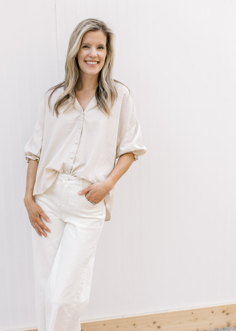 Model wearing white pants with a taupe button up top with 3/4 elastic sleeves and a collar.