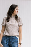 Model wearing a taupe top with neutral colored pattern with a smocked neck and short sleeves.