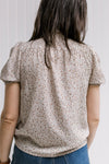 Back view of model wearing a taupe top with neutral colored pattern, smocked neck and short sleeves.