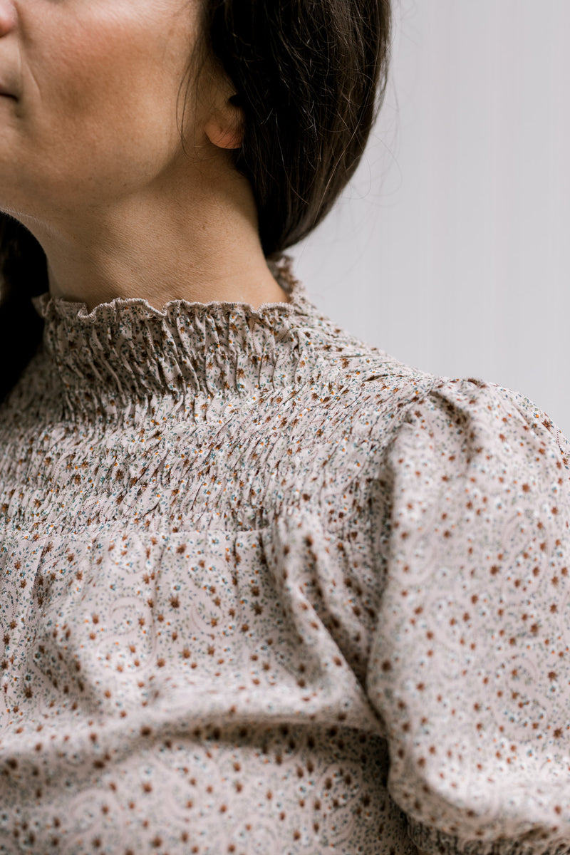 Close up of smocked detail and bubble short sleeves on a taupe top with a neutral color pattern. 