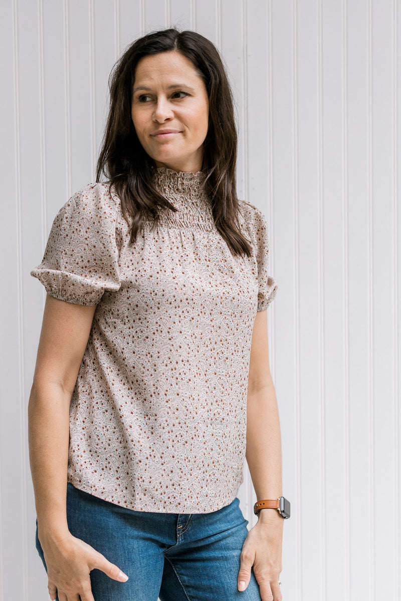Model wearing jeans with a taupe top with a neutral pattern, bubble short sleeves and a smocked neck