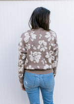 Back view of Model wearing a taupe sweater with cream flowers and long sleeves