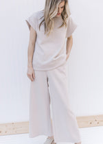 Model wearing a taupe textured set with wide leg pants and a top with extended cap sleeves. 