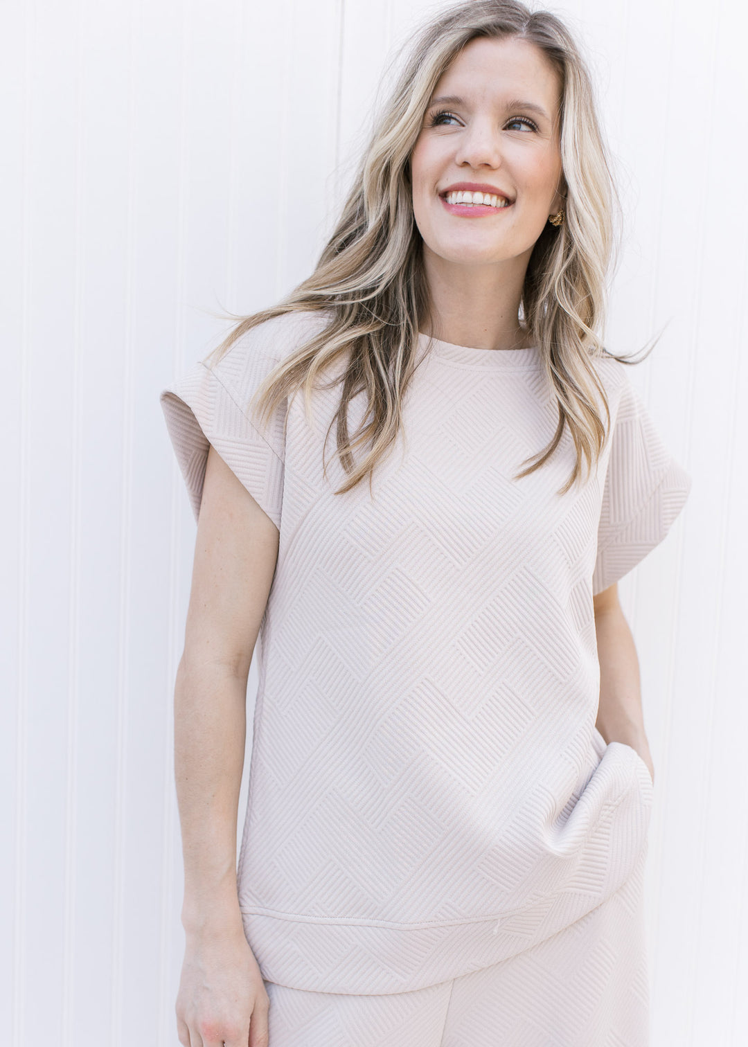 Model wearing a textured taupe top with extended cap sleeves, part of a set with wide leg pants.