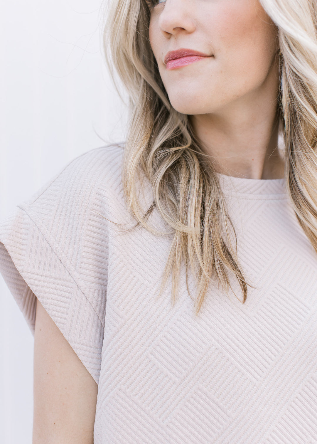Close up of textured material and extended cap sleeves of a taupe top that is part of a set. 