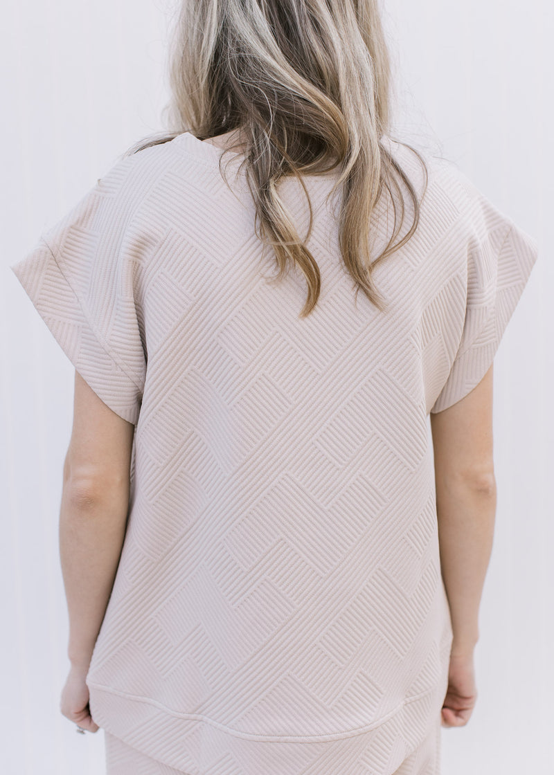 Back view of Model wearing a textured taupe top with cap sleeves, part of a set with wide leg pants.