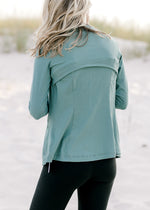 Back view of a model wearing a teal zip up athletic jacket. 