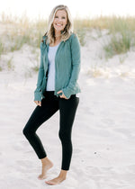 Model wearing a teal zip up jacket with black leggings and a white top. 