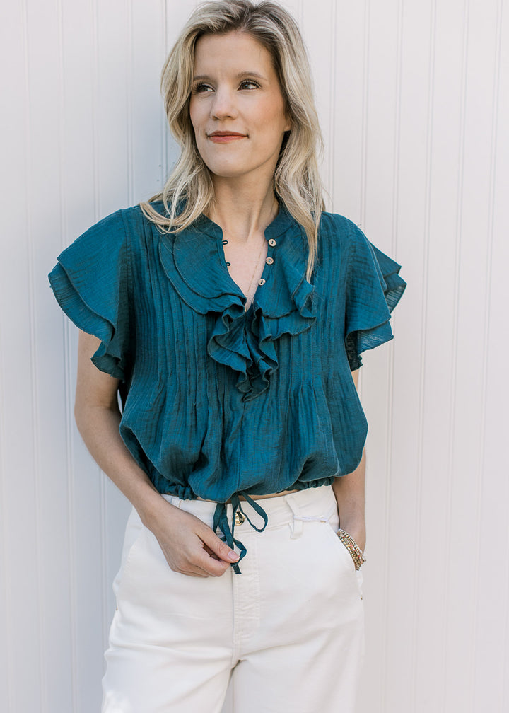 Model wearing a teal v-neck with a crop, drawstring waist, a pleated bodice and ruffle cap sleeves.