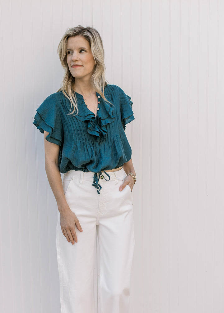 Model wearing a teal v-neck with double ruffle a pleated bodice and ruffle cap sleeves.