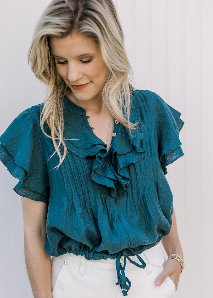 Model wearing a teal v-neck with wooden buttons, a cropped fit and ruffle cap sleeves.