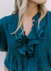 Close up of double ruffles and wooden buttons on a teal v-neck with cap sleeves and crop fit.