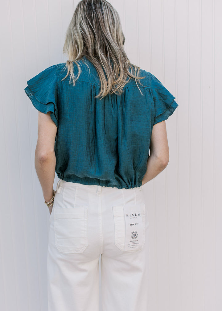 Back view of Model wearing a teal cropped top with double ruffle cap sleeves. 
