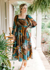 Model wearing clogs and a brown dress with teal, tan and brick floral, long sleeves and smocked back