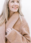 Close up of flap collar and long sleeves on a cozy camel colored jacket with a polyester material. 