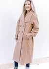 Model wearing a knee length camel colored jacket with a double breast, flap collar and long sleeves.