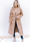 Model wearing a camel, double breasted knee length jacket unbuttoned with long sleeves. 