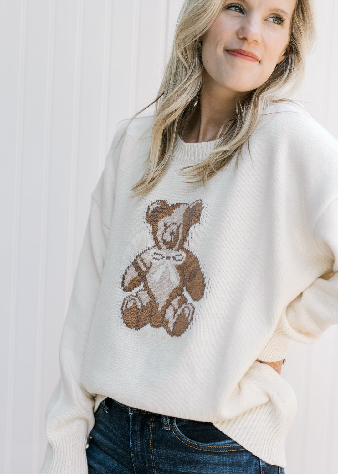 Model wearing a cozy cream sweater with a brown bear on the front, long sleeves and a round neck. 