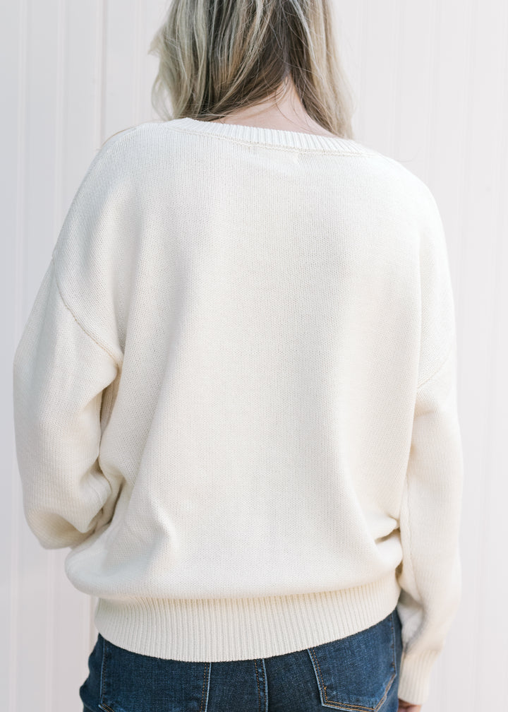Back view of Model wearing a cream sweater with a brown bear, long sleeves and a round neck. 