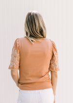 Back view of Model wearing a burnt orange top with a cream floral embroidery on short sleeves. 